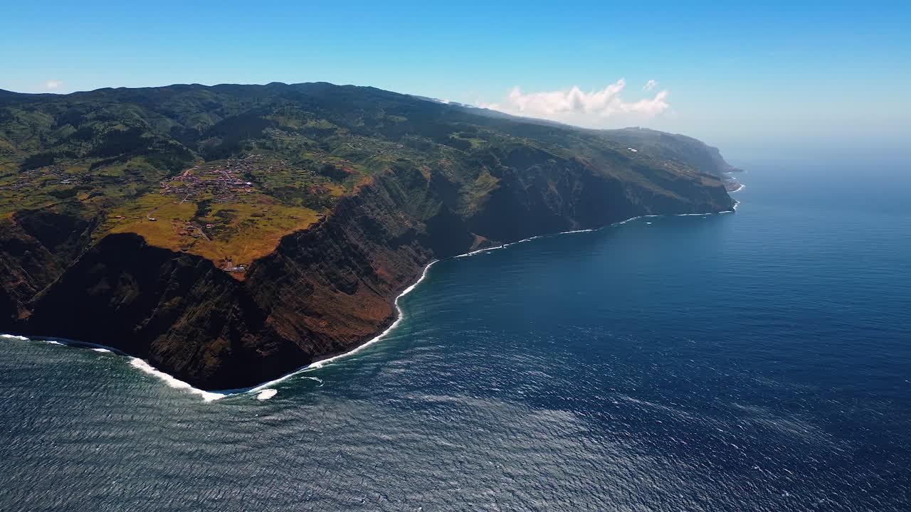 Beautiful deep blue waterscape of the Atlantic Ocean at the rocky shore of the Madeira Islands, Portugal. Slopes of the mountains with village houses on. Aerial view.