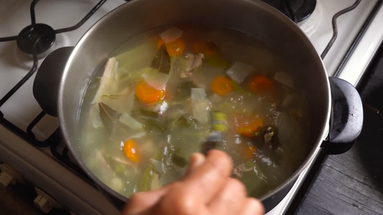 cocinar y revolver una nutritiva sopa de pollo con zanahorias y verduras de hoja en una olla