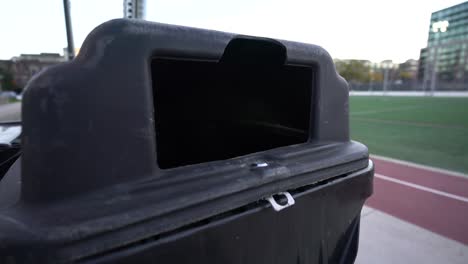 Hand-throwing-out-disposing-dog-poop-waste-bag-in-bin-in-park,-handheld-close-up