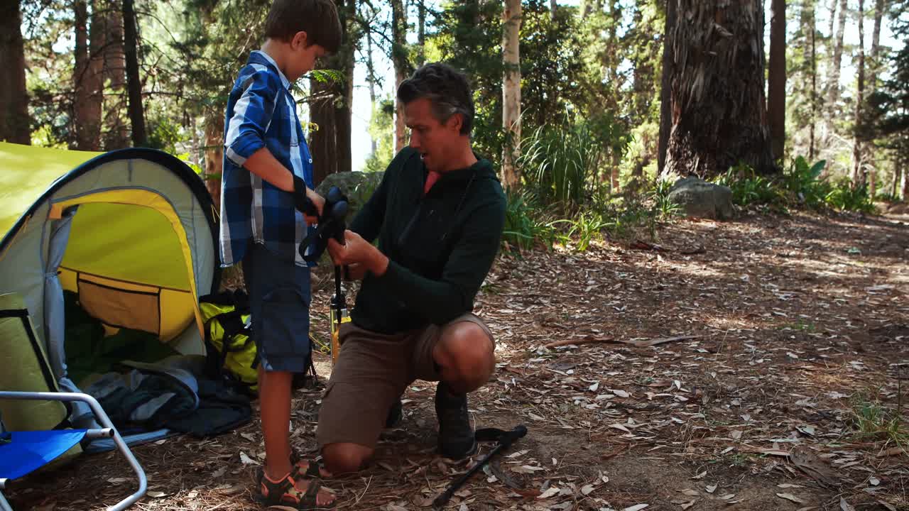 padre enseñando a su hijo a usar la barra de trekking fuera de la tienda