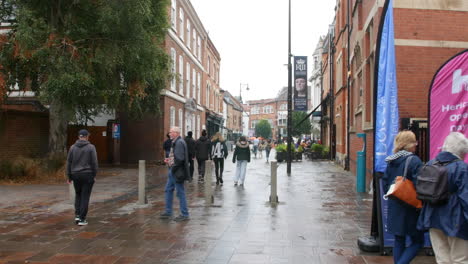 people are walking along a wet, pedestrian street lined with brick buildings and banners promoting the richard iii visitor centre in leicester.