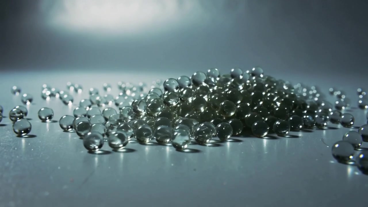Rolling clear beads after small motion forming mound on studio table, overhead light casting sheen