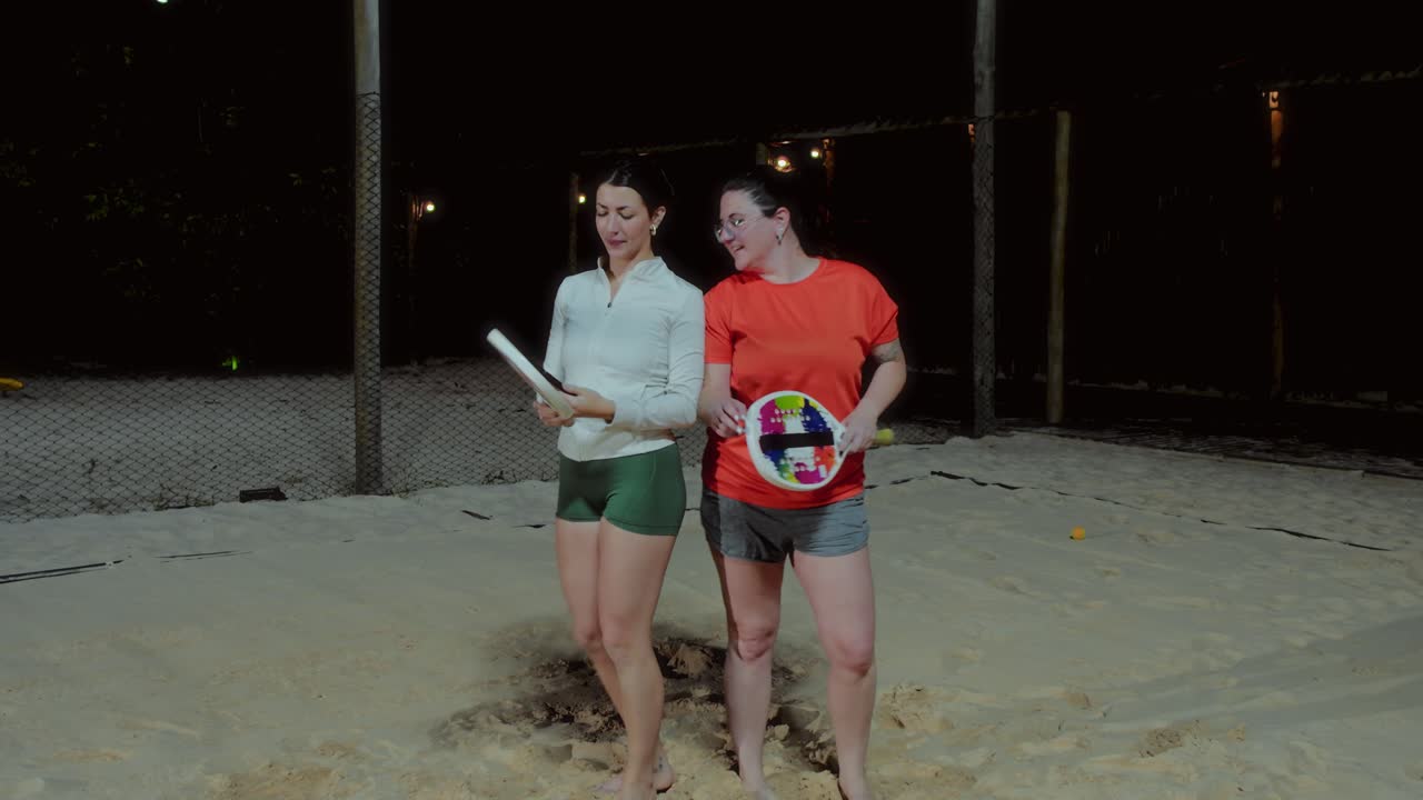 Women playing beach tennis, taking selfies, and checking phones at night