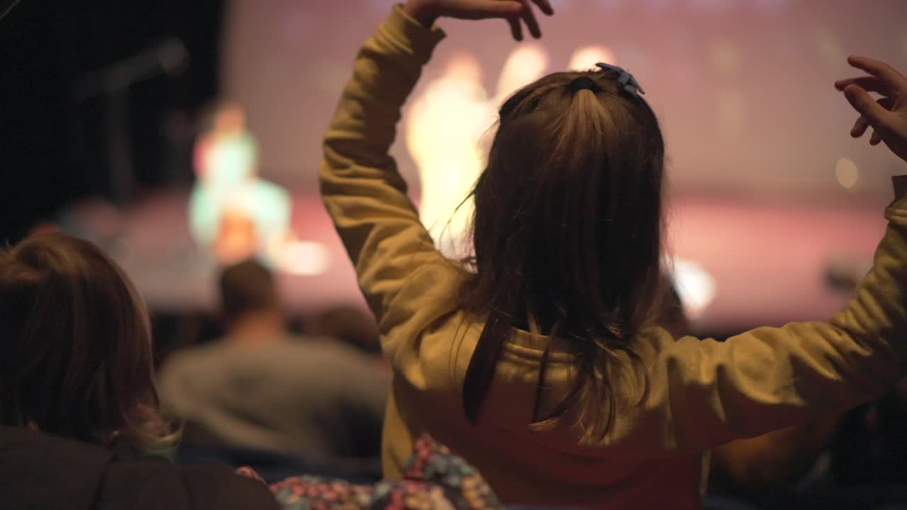 niño bailando a cámara lenta en la audiencia en un teatro viendo un concierto en vivo, niñita agitando los brazos en el aire