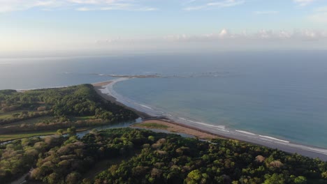 Costa-Rica-drone-top-view-showing-sea,-shore-and-palm-tree-forest-in-the-pacific-ocean-with-a-whale-tale-shape-beach