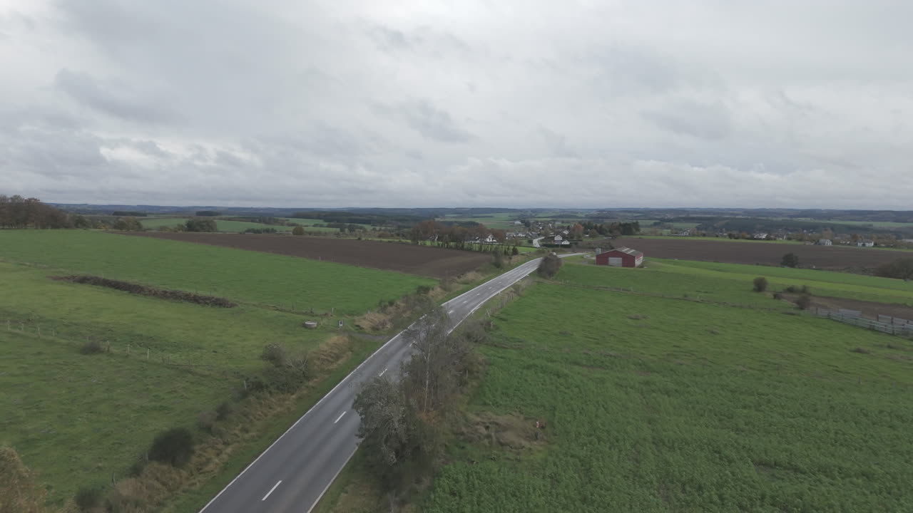 회색 날의 벨기에 풍경의 드론 촬영으로 빠르게 움직이는 구름과 도로와 마을이 배경에 있습니다.
