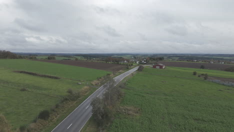 drone shot of a belgian landscape on a grey day with fast moving clouds and a road and village in de background log