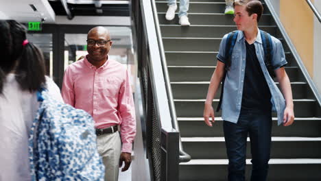 male high school student talking with teacher in busy corridor