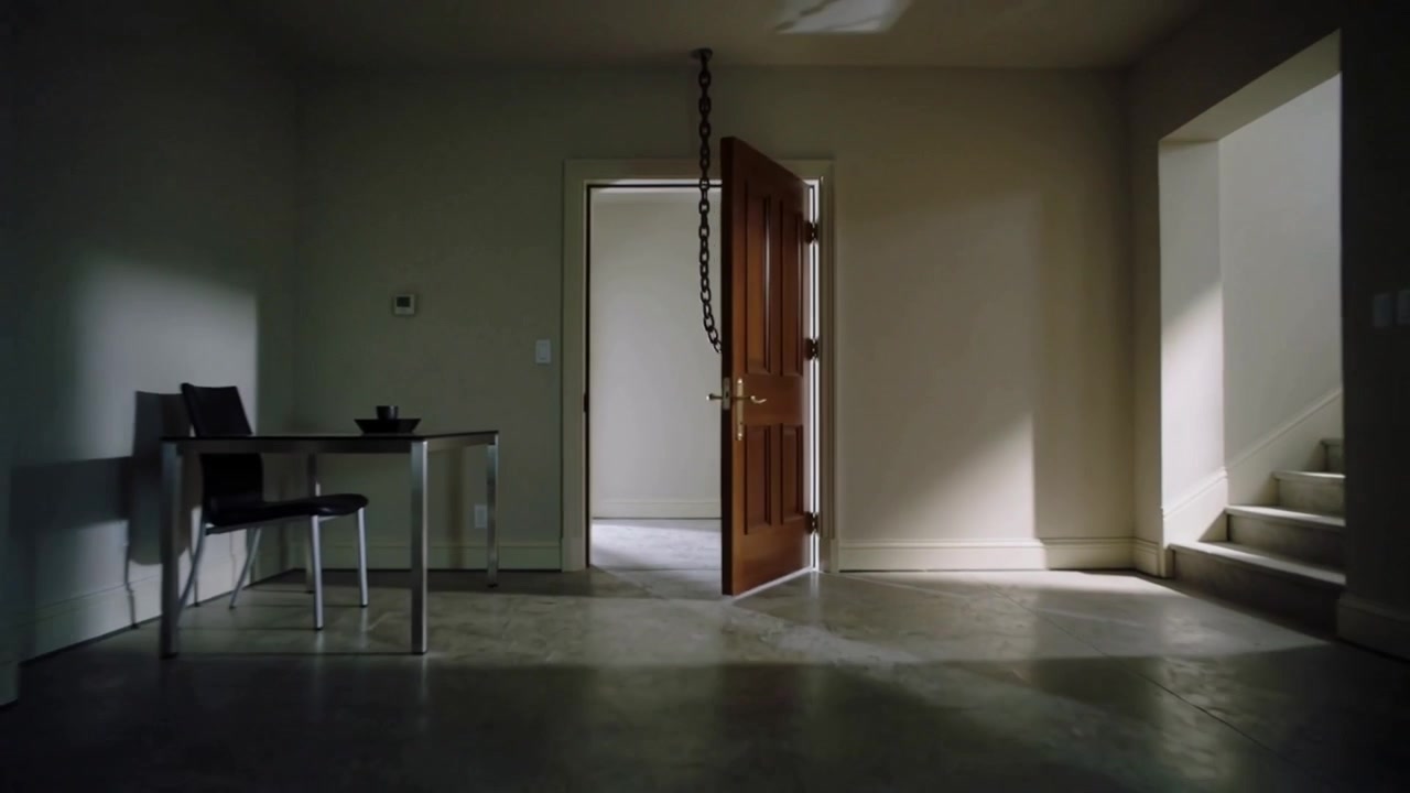 Rivelando una porta di legno a sei pannelli che si apre verso l'interno mentre la telecamera si allontana in casa, con una catena appesa