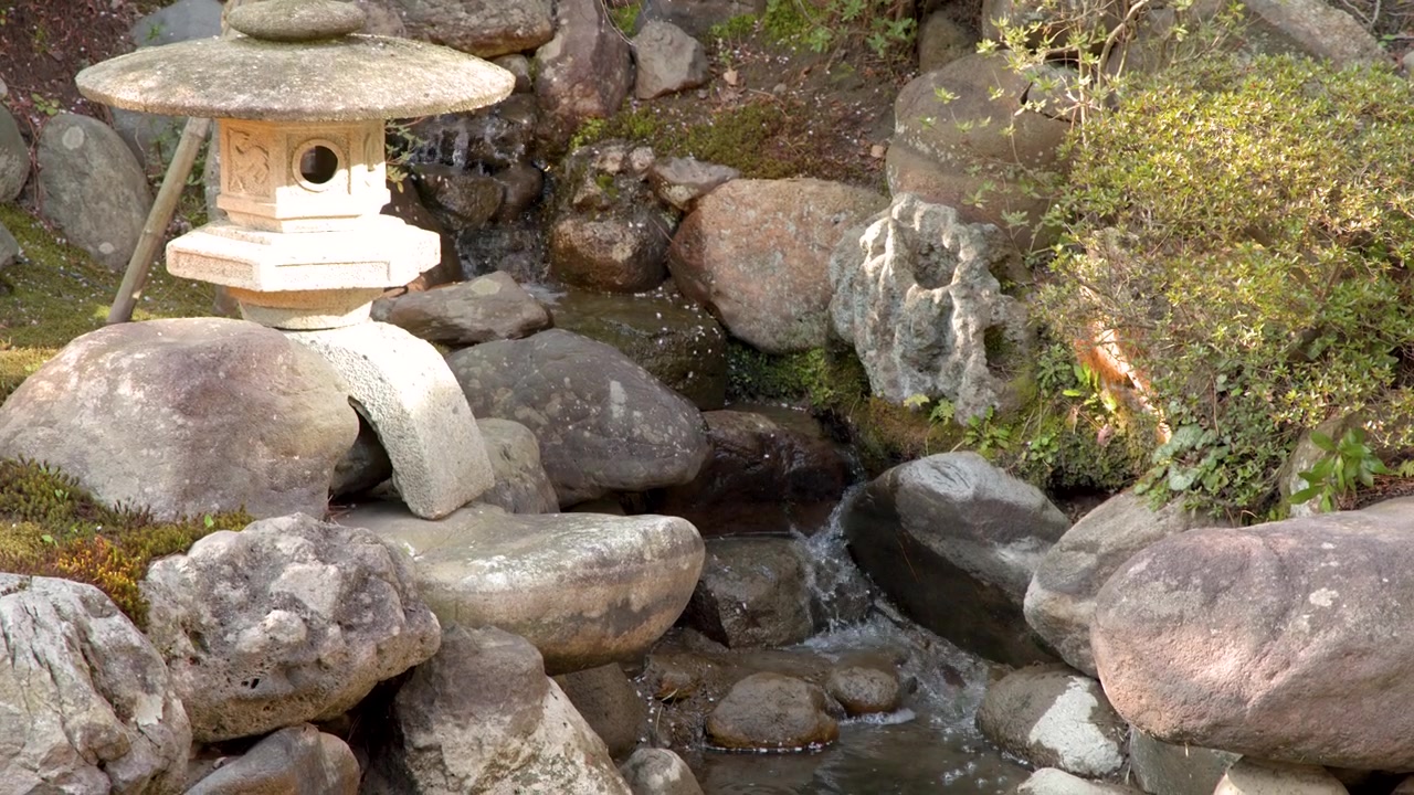 Un'inquadratura statica di una lanterna toro in pietra accanto a un ruscello che scorre a Kanazawa.