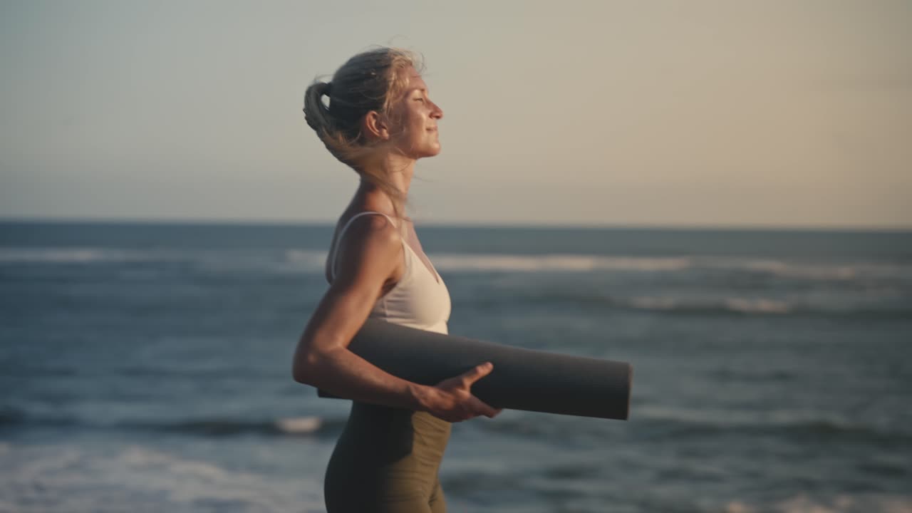 la donna di yoga in forma tiene il tappetino camminando lungo la costa tropicale, prendendo un concetto di pausa