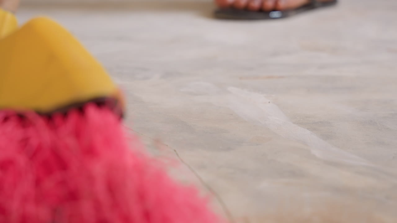 Cleaning in progress. Detailed shot of floor sweeping action. Focus on precise dust removal from tiled surface. Domestic cleaning scene showing person sweeping debris with focused attention