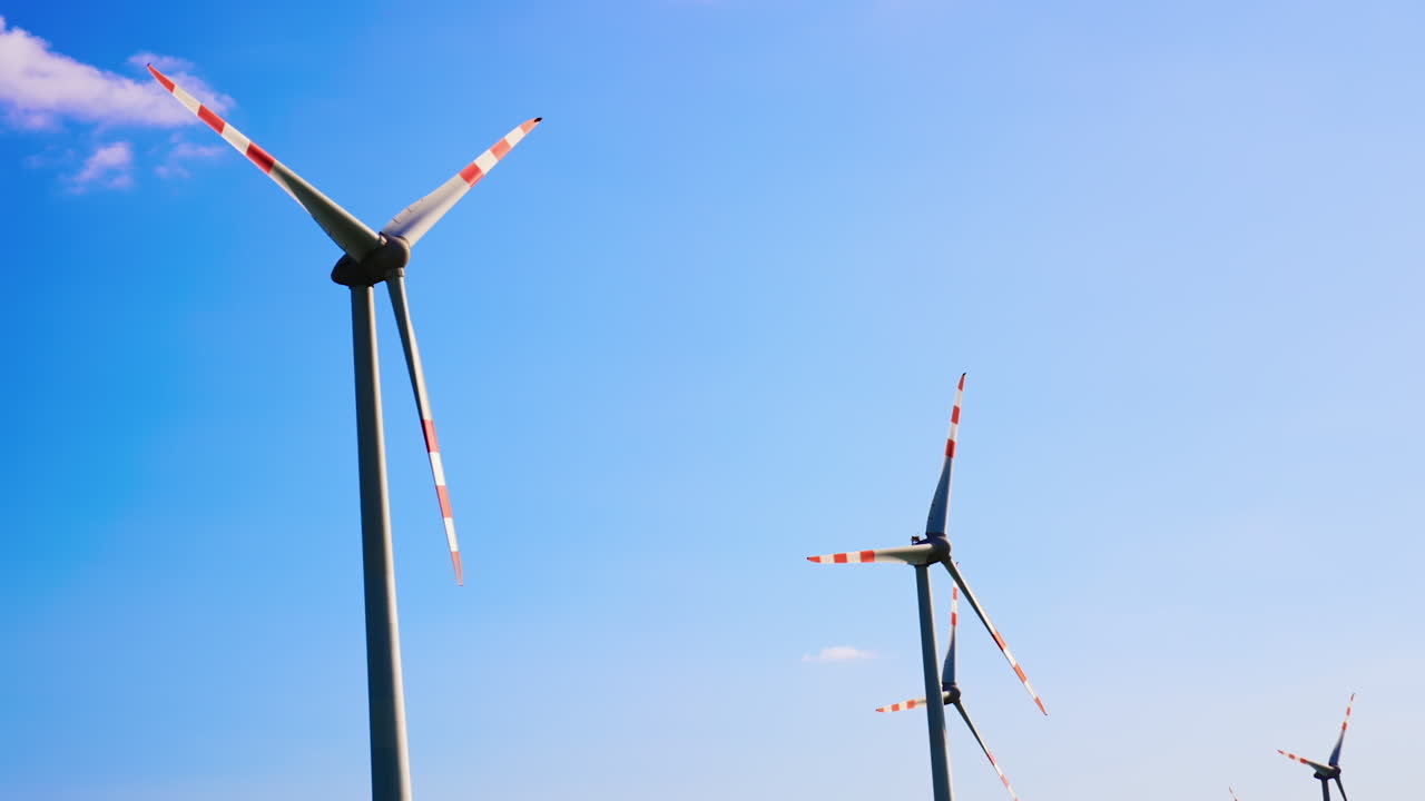 Wind turbines producing energy. Tall wind turbines spin against a clear blue sky, producing sustainable energy in a rural landscape during daytime