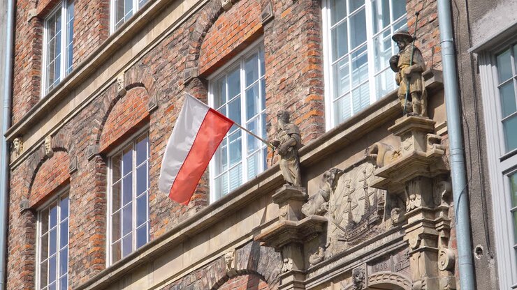 Bandiera polacca che sventola da un edificio storico ornato con statue e mattoni rossi sotto un cielo sereno