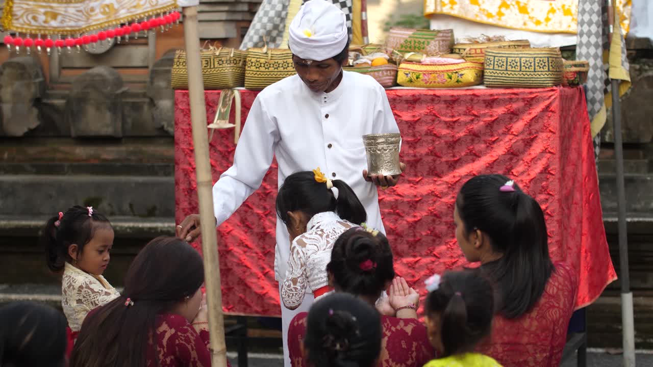 Hindu priest pours water into hands of women and children and sprinkle their heads at temple event. Culture and religious beliefs of Indonesia. Spirituality and ceremony of Hinduism.