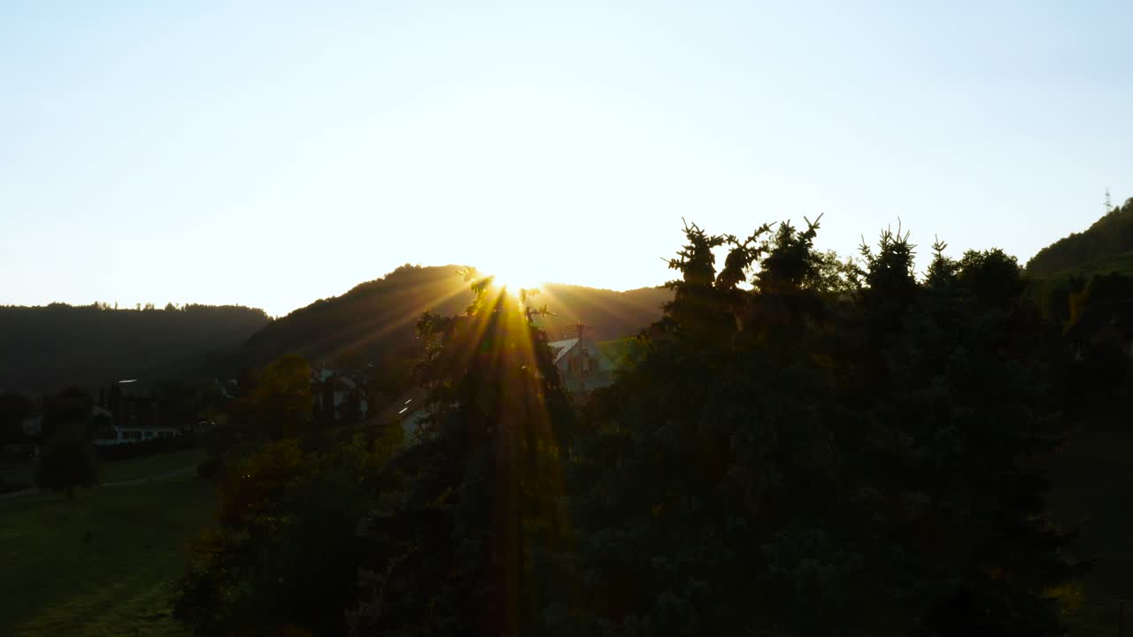 스위스 시골의 작은 마을에 있는 나무 사이로 태양 플레어가 빛나는 일부 소나무 위로 날아갑니다.