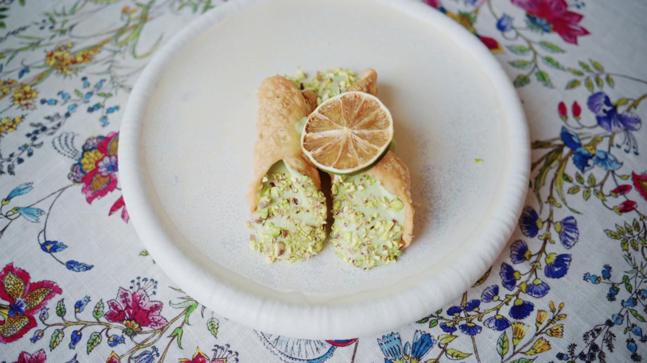 Primer plano de cannoli relleno de crema de pistacho cubierto con una rodaja de lima en un plato en un restaurante italiano