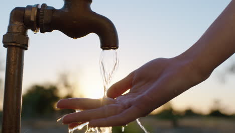 Nahaufnahme-Einer-Frau,-Die-Sich-Bei-Sonnenaufgang-Auf-Ländlichem-Ackerland-Die-Hände-Unter-Leitungswasser-Mit-Frischem-Wasser-Wäscht