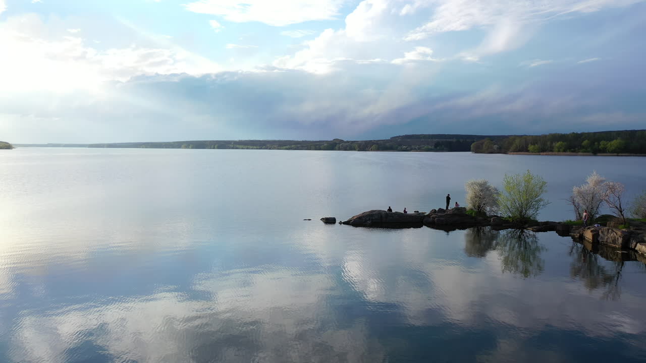 Beautiful river on nature landscape in spring. People rest near the water on stones in springtime. Blooming trees on a bank of the river.