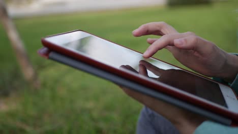 young beautiful slim woman with long blonde hair in green shirt sits on the ground and using tablet pc over background the park. girl on the square touching screen and smile