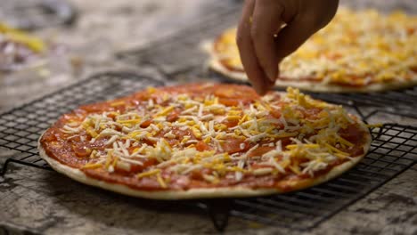 Close-up-of-hand-applying-shredded-cheese-ingredient-on-homemade-uncooked-pizza