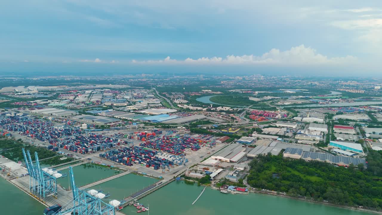 Aerial view of Northport in Klang, Malaysia, revealing container terminals, port infrastructure, and a sprawling cityscape under a partly cloudy sky. UHD.