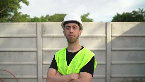 an engineer, wearing a white hard hat, crosses his arms over his chest - medium close up