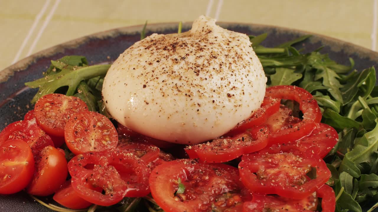 Burrata or Mozzarella cheese on fresh tomatoes and green arugula on plate close-up. From Italian cow's milk cheese made from mozzarella and cream.The outer casing is solid cheese, while the inside contains stracciatella and clotted cream, giving it an unusual, soft texture.