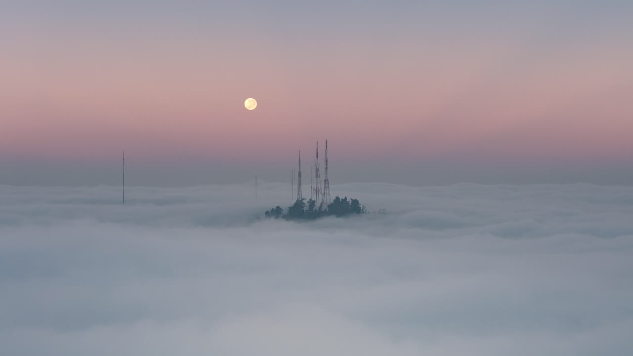 Hyperlapse shot of antennas on a hill in Santiago with the moon visible above moving clouds during twilight