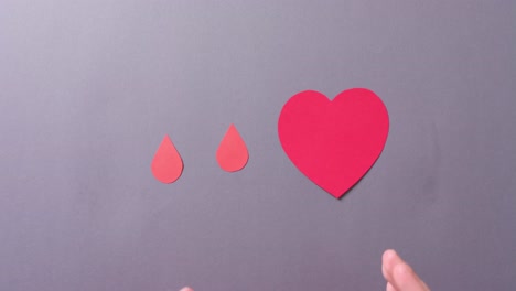 manos de una mujer caucásica protegiendo el corazón y gotas de sangre en fondo gris, cámara lenta
