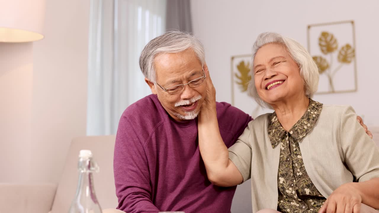 An elderly couple shares laughter and affection in a cozy living room setting with warm lighting