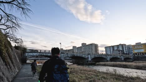 individuals walking by a river under a bridge