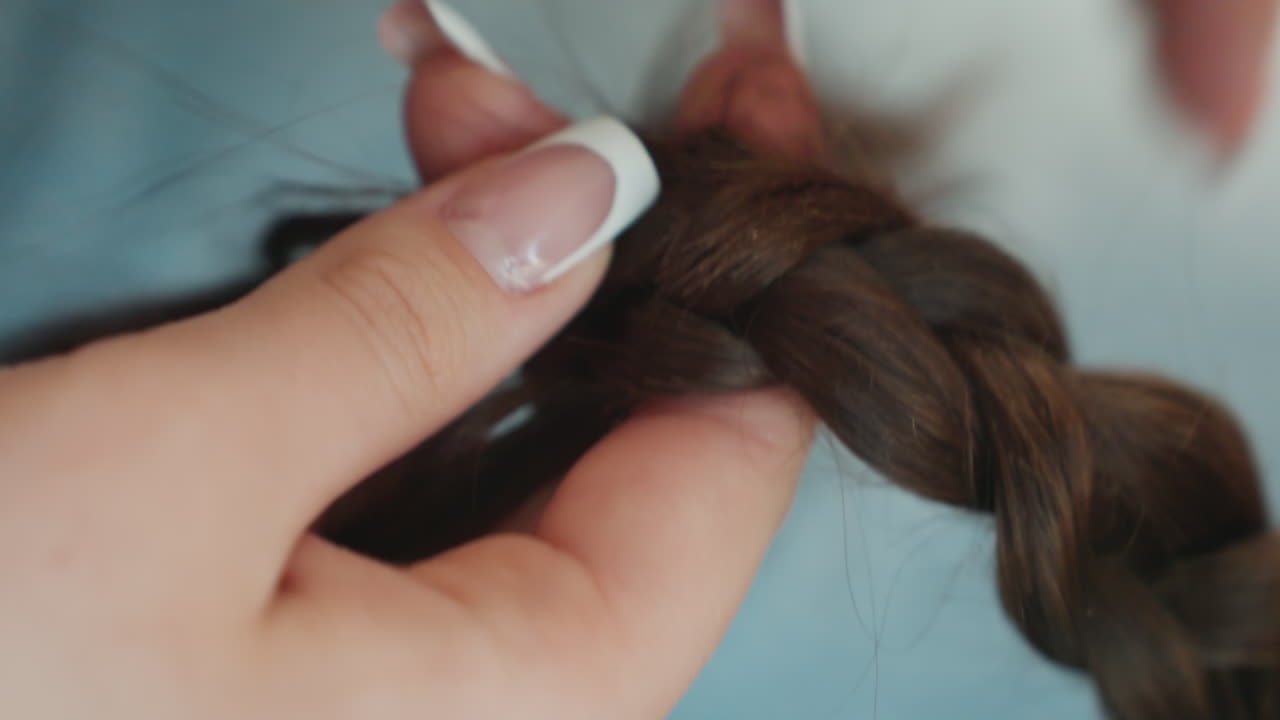 CloseUp Hands Braiding Brown Hair With French Manicure, Precise Fingertip Movements Weaving Strands Into Braid, Salon Technique And Grooming Routine, Polished Nails And Textured Strands, Focused