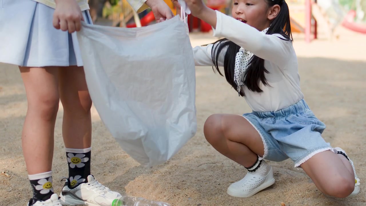 Two young Thai girls volunteer by collecting plastic waste into bags at Lumpini Park, Bangkok.