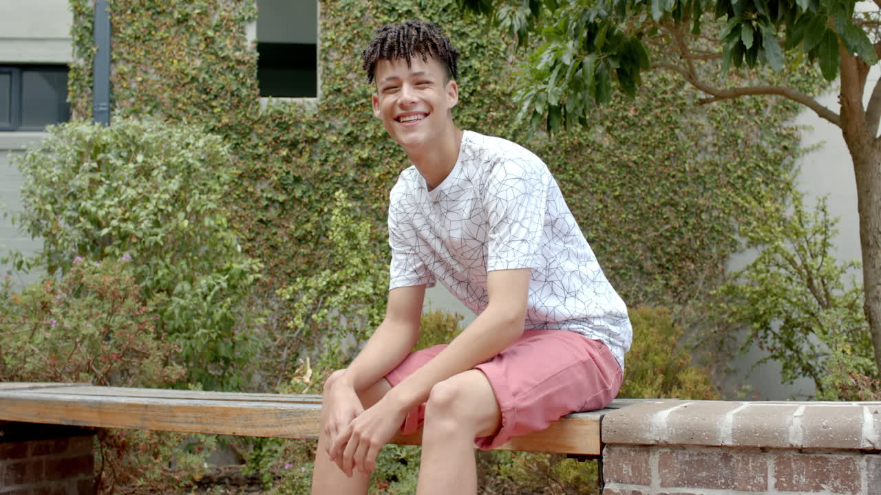 Teenage biracial boy sitting on a bench outdoors, with copy space