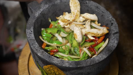 cook adds sauted peppers onions and chicken fajita to sizzling hot molcajete lava rock bowl, slow motion close up 4k