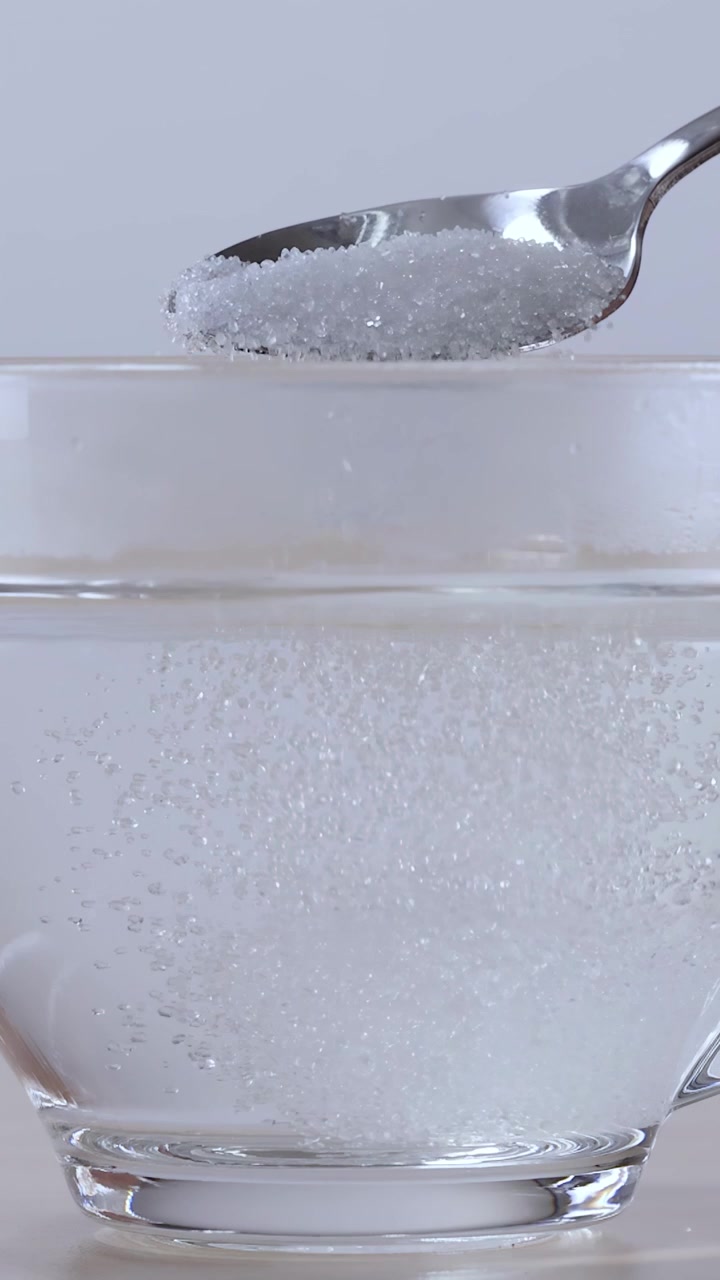 Primo piano di acqua versata e zucchero mescolato in una tazza di vetro trasparente con un cucchiaio