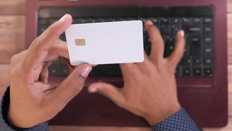 person holding a credit card and typing on a laptop