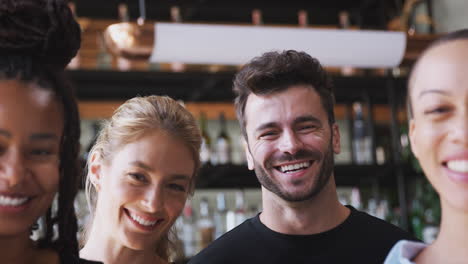 portrait of smiling female owner of restaurant bar with team of waiting staff standing by counter