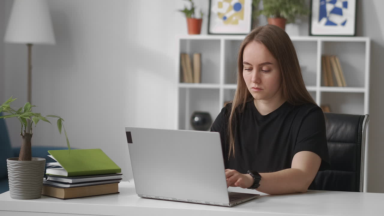 mujer seria vestida con una camiseta negra está trabajando con una computadora portátil en la oficina de casa escribiendo en chat en línea en redes sociales smm o seo especialista en trabajo remoto contemporáneo