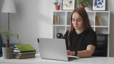 Ernsthafte-Frau-In-Schwarzem-T-Shirt-Arbeitet-Mit-Laptop-Im-Home-Office-Und-Tippt-Im-Online-Chat-In-Sozialen-Netzwerken-SMM-Oder-SEO-Spezialistin,-Zeitgenössische-Fernarbeit