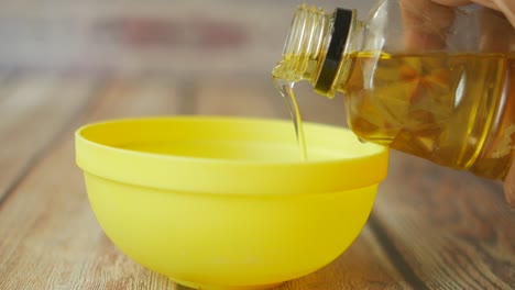 pouring oil into a yellow bowl on a wooden table