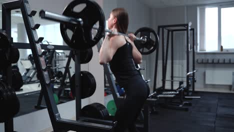 a strong woman in black sportswear performs an exercise with a barbell in the gym. squatting.