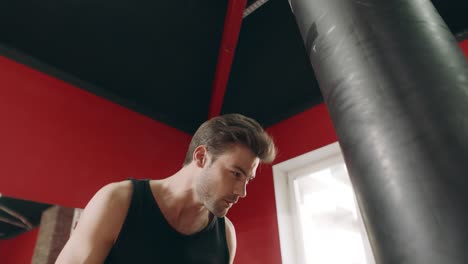 boxer man kicking combat bag in gym low angle view.