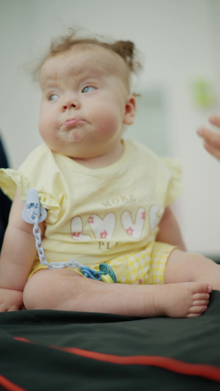 Curious baby girl with blue eyes and saliva on her mouth, looking up while being held by an adult