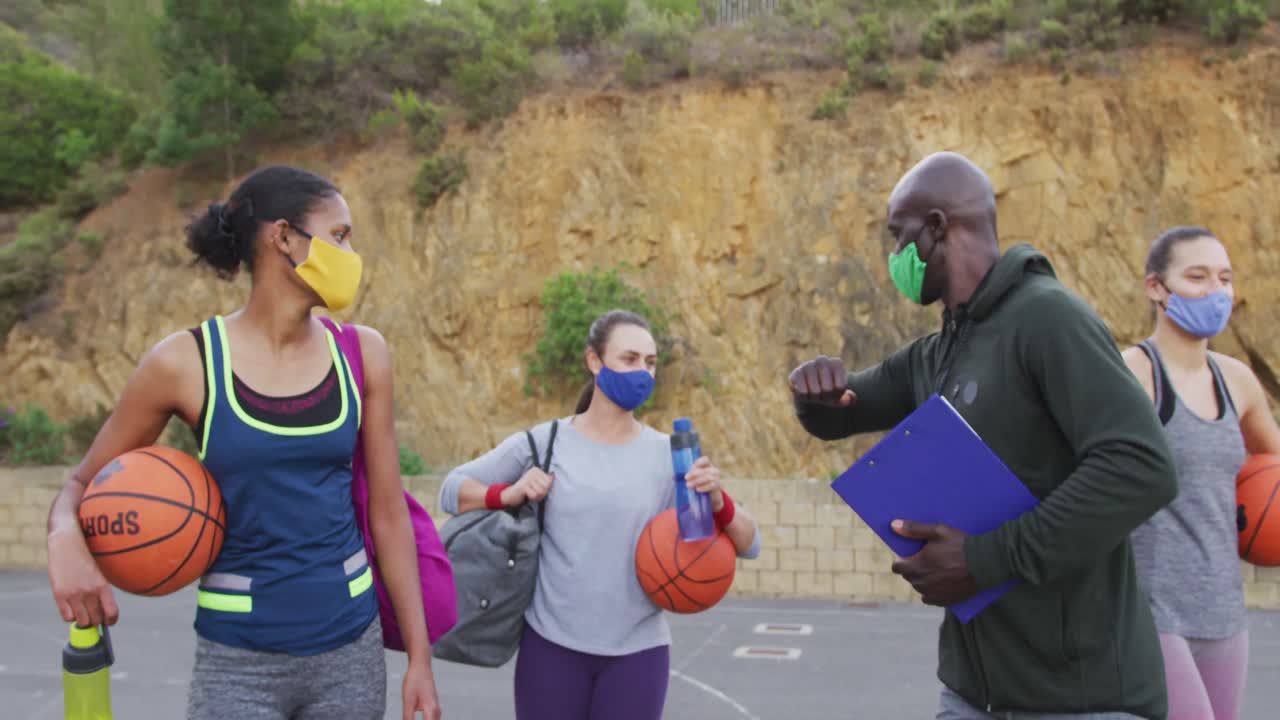 Diverse female basketball team and male coach wearing face masks greeting with elbows