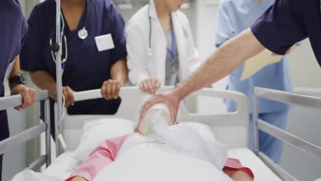 video of diverse group of medical workers pushing patient on drip and ventilator in hospital bed