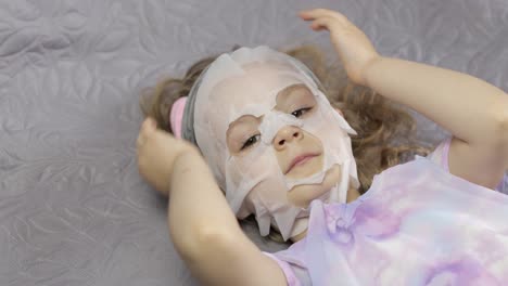 teen girl applying moisturizing face mask. child kid take care of skin with cosmetic facial mask