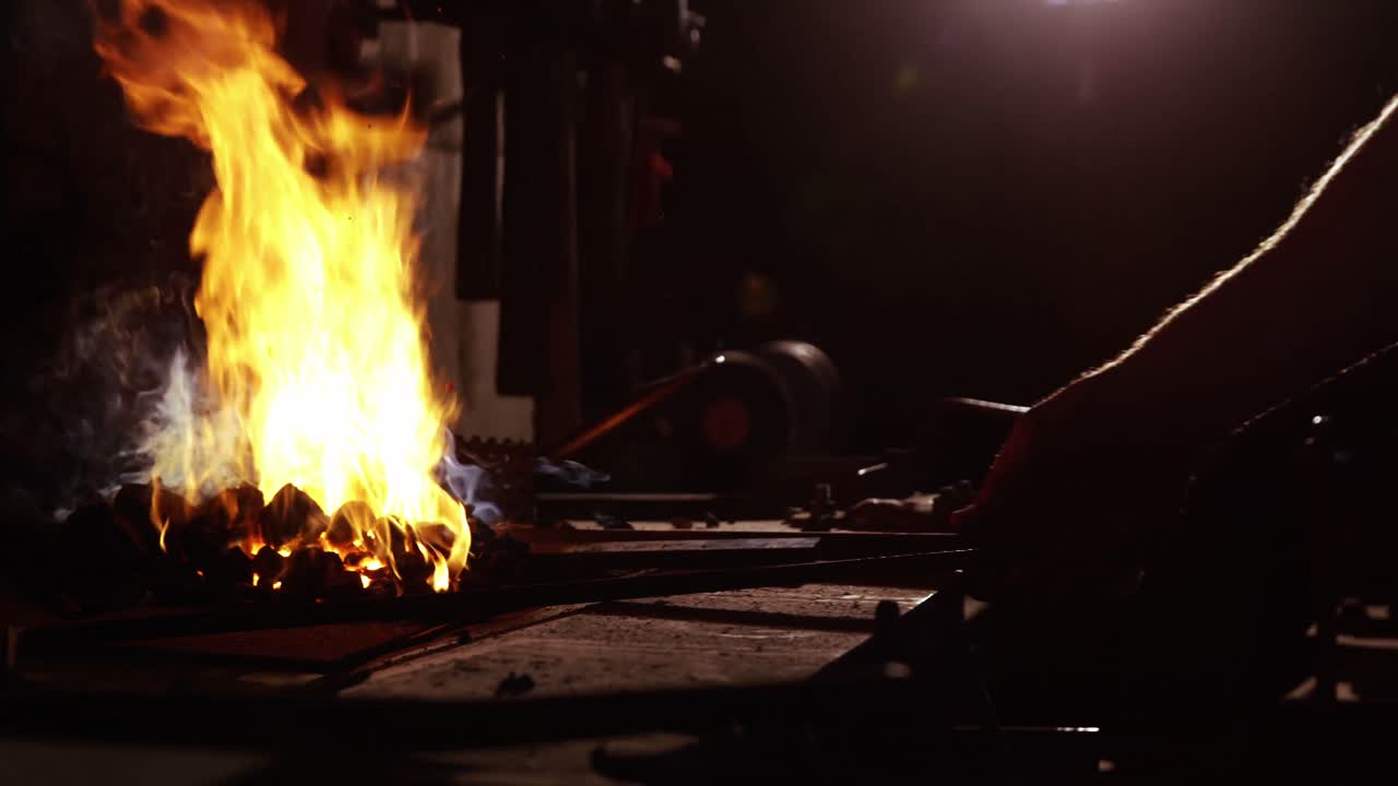 冶師の手が火で鉄の棒を加熱する