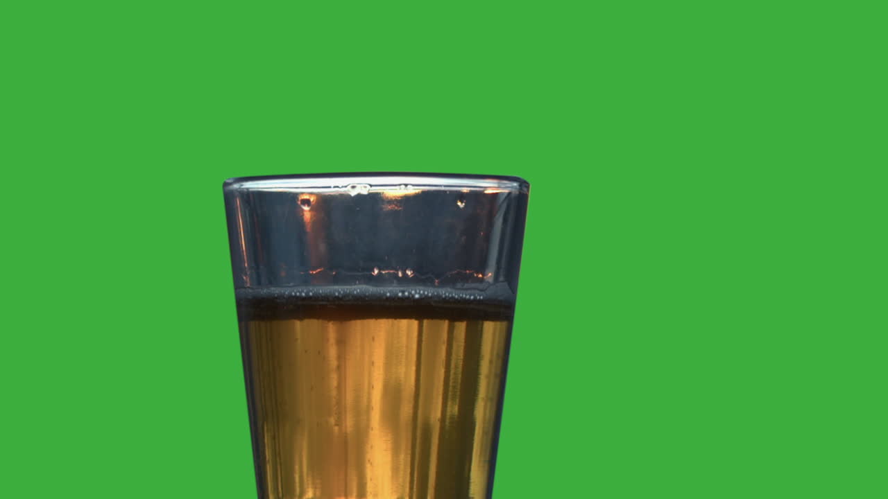 las burbujas se elevan en un vaso de cerveza dorada pálida contra el fondo de la pantalla verde